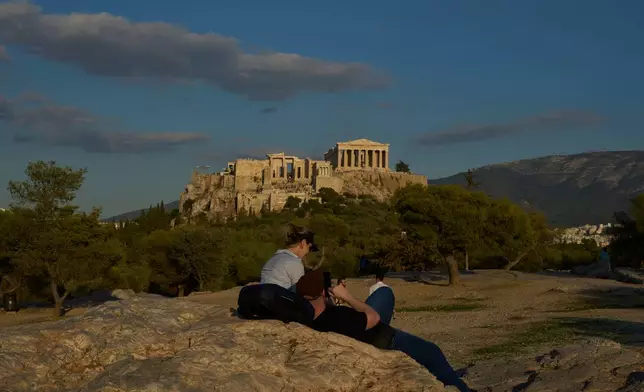 Tourist rest at Pnyx as the 5th century B.C. Parthenon temple stands free of scaffolding on the Acropolis hill in Athens, Friday, Oct. 10, 2025, after the removal of restoration structures that had covered parts of the ancient monument for decades.(AP Photo/Petros Giannakouris)