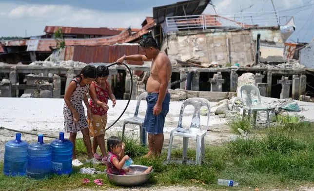 A man takes a bath with his daughters beside damaged structures due to a recent strong earthquake in Bogo, Cebu Province, Central Philippines on Friday, Oct. 3, 2025. (AP Photo/Aaron Favila)