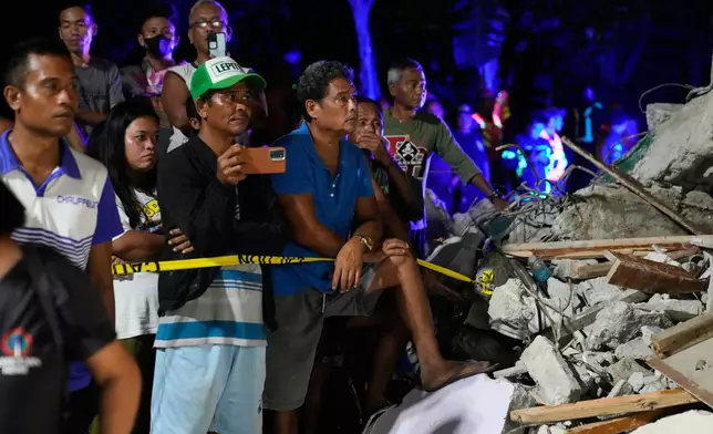 Residents look as rescuers search for survivors at a collapsed building, Wednesday, Oct. 1, 2025 after a strong earthquake struck Bogo city, Cebu Province, Central Philippines. (AP Photo/Aaron Favila)