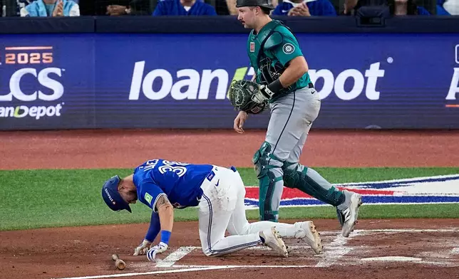 Toronto Blue Jays' Nathan Lukes is slow to get up after fouling the ball off his leg as Seattle Mariners catcher Cal Raleigh, right, looks away during the first inning in Game 1 of baseball's American League Championship Series, Sunday, Oct. 12, 2025, in Toronto. (AP Photo/David J. Phillip)