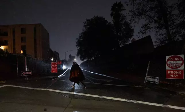 A homeless person walks under gusty showers in East Los Angeles early morning Tuesday, Oct. 14, 2025. (AP Photo/Damian Dovarganes)