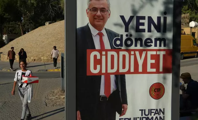 People walk past a campaign poster of Turkish Cypriot candidate Tufan Erhurman ahead of the Turkish Cypriot elections in the Turkish occupied northern part of divided Nicosia, Cyprus, Friday, Oct. 17, 2025. (AP Photo/Petros Karadjias)