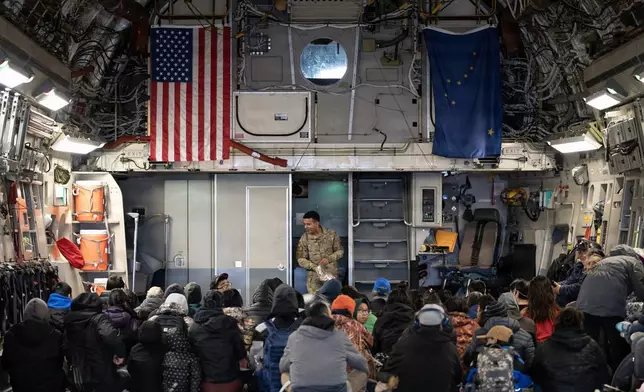 In this photo provided by the Alaska National Guard, Alaska Air National Guard Staff Sgt. Angel Reyes distributes hearing protection to passengers while evacuating Alaskans displaced in the aftermath of Typhoon Halong out of Bethel, Alaska, Wednesday, Oct. 15, 2025. (Alaska National Guard via AP)