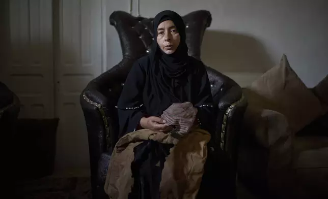 Wafa Jazar, 42, sits for a portrait, holding the clothes that her 14-year-old son, Ahmad Jazar, was wearing when he was shot by Israeli soldiers, at their home in the West Bank village of Sebastia, March 11, 2025. (AP Photo/Leo Correa)