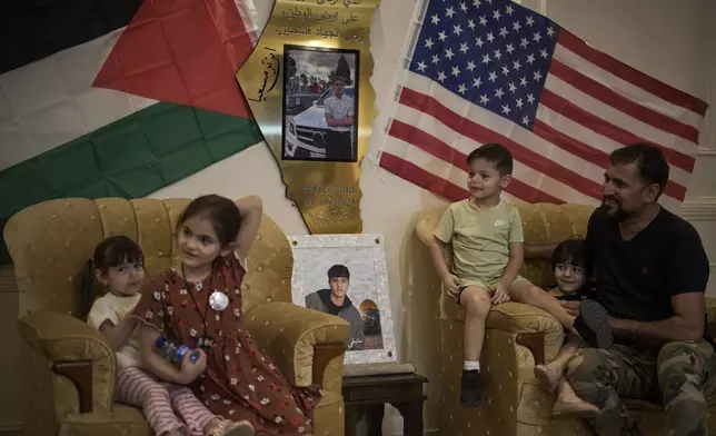 Mohammed Rabee, 48, sits with his grandchildren beside photos of his 14-year-old son, Amer Rabee, who was killed by Israeli soldiers while in a roadside thicket in the West Bank town of Turmus Ayya, April 22, 2025. (AP Photo/Leo Correa)