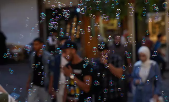 Soap bubbles float in the air as people walk through the old city of Damascus, Syria, Thursday, Oct. 2, 2025. (AP Photo/Hussein Malla)