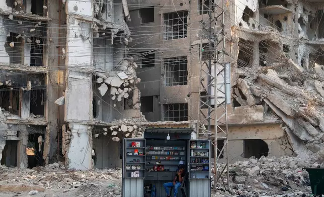 A man waits for customers at a stall beside war-damaged buildings ahead of a parliamentary election set to take place Sunday, in the Damascus suburb of Daraya, Syria, Saturday, Oct. 4, 2025. (AP Photo/Omar Sanadiki)