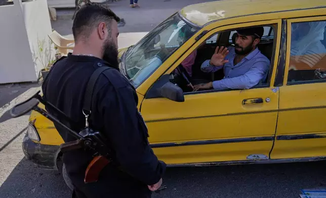 A taxi driver waves to a Syrian government security man at a checkpoint, in the southern Damascus suburb of Jaramana, Syria, Friday, Oct. 3, 2025. (AP Photo/Hussein Malla)