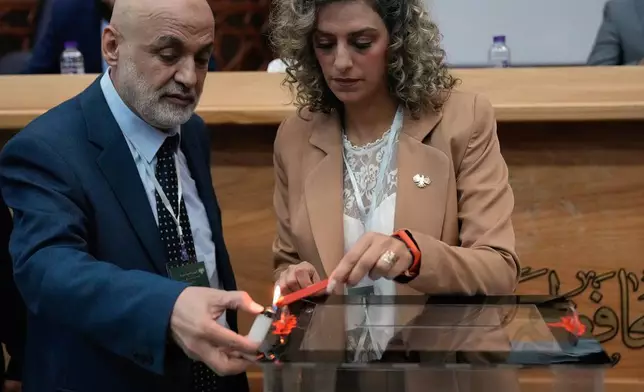 Syrian election officials burn red wax to stamp a ballot box ahead of the parliamentary elections at Latakia's Governor ballot station, in the coastal city of Latakia, Syria, Sunday, Oct. 5, 2025. (AP Photo/Hussein Malla)