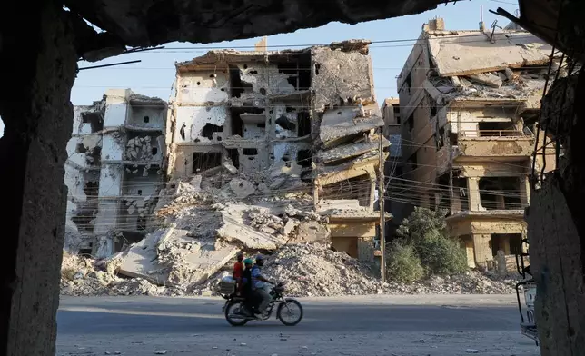 Residents ride a motorcycle past war-damaged buildings in the Damascus suburb of Daraya, Syria, Saturday, Oct. 4, 2025, ahead of a parliamentary election set to take place Sunday. (AP Photo/Omar Sanadiki)