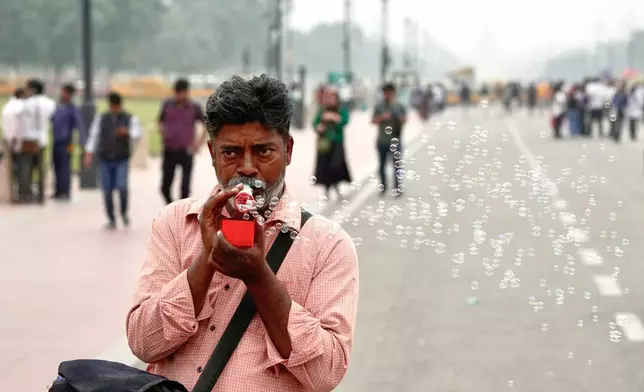 A street hawker blows soap bubbles to advertise his wares on a street enveloped in smog, in New Delhi, India, Tuesday, Oct. 28, 2025. (AP Photo/Manish Swarup)