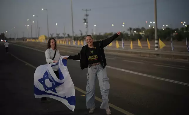 People wave Israeli flags as they gather prior to the release of Israeli hostages held in Gaza, in front of a military base near Reim Area, southern Israel, on Monday, Oct, 13, 2025. (AP Photo/Leo Correa)