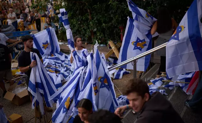 Volunteers prepare Israeli flags as people gather at a plaza known as hostages square, in Tel Aviv, Israel, Sunday, Oct. 12, 2025. (AP Photo/Emilio Morenatti)