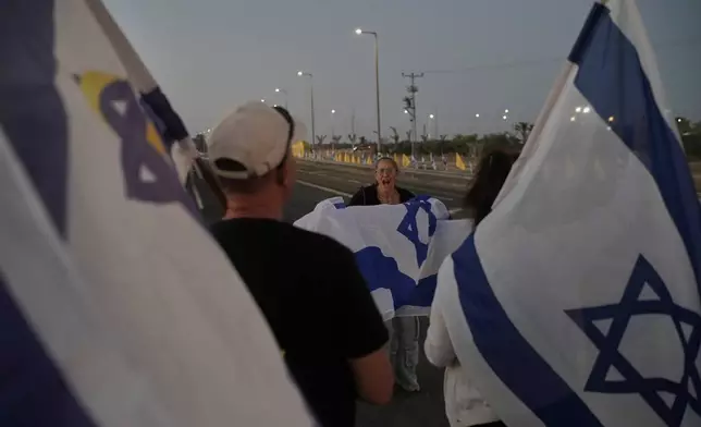 People hold Israeli flags as they gather prior to the release of Israeli hostages held in Gaza, in front of a military base near Reim Area, southern Israel, on Monday, Oct, 13, 2025. (AP Photo/Leo Correa)