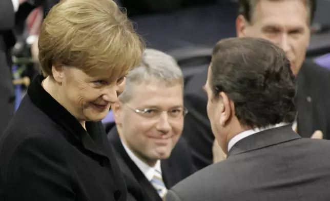 FILE - Newly elected German chancellor Angela Merkel, left, is congratulated by her predecessor Gerhard Schroeder, right, as lawmakers Norbert Roettgen and Michael Glos, background right, look on after her election in the parliament in Berlin, on Nov. 22, 2005. (AP Photo/Fritz Reiss, File)