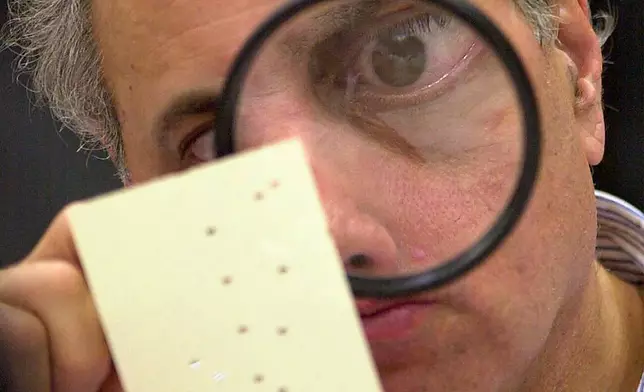 FILE - Broward County canvassing board member Judge Robert Rosenberg using a magnifying glass to examine a disputed ballot at the Broward County Courthouse in Fort Lauderdale, Fla., on Nov. 24, 2000. (AP Photo/Alan Diaz, File)