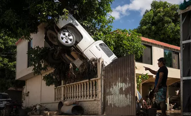 A pickup truck hangs over a fence in Poza Rica, Veracruz state, Mexico, Sunday, Oct. 12, 2025, after rain and flooding. (AP Photo/Felix Marquez)