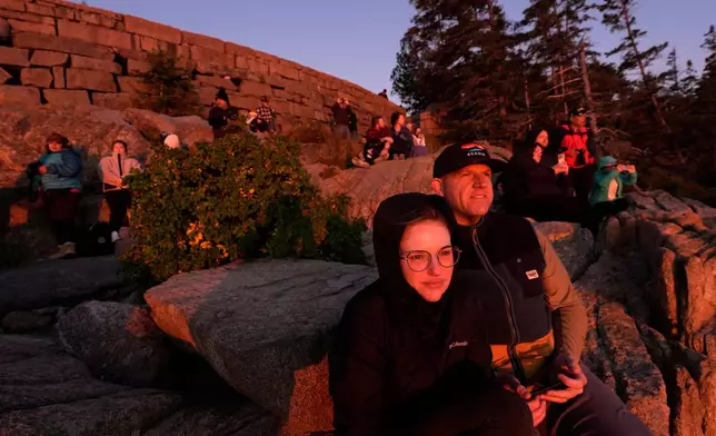 Kaitlin and Kurt Wilhelm, of Sandusky, Ohio, foreground, and others gather on the rocky coast to watch the sunrise, Wednesday, Oct. 1, 2025, in Acadia National Park, Maine. (AP Photo/Robert F. Bukaty)