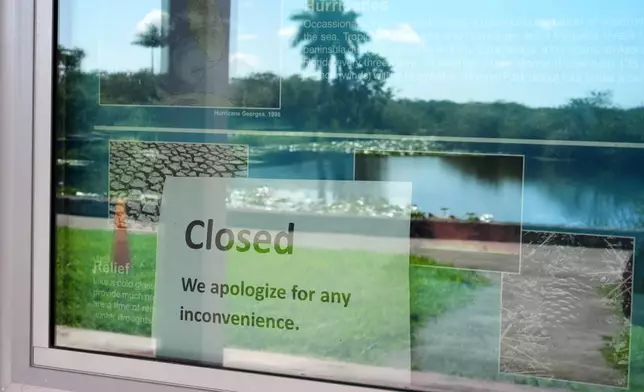 A sign alerting visitors that the Royal Palm Visitor Center is closed hangs in a display case reflecting the landscape, inside Florida's Everglades National Park, Wednesday, Oct. 1, 2025. (AP Photo/Rebecca Blackwell)