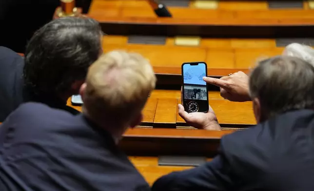 Lawmakers look on a phone at the National Assembly the results of a no-confidence motion vote on French Prime Minister Sébastien Lecornu's government in Paris, Thursday, Oct. 16, 2025. (AP Photo/Thibault Camus)