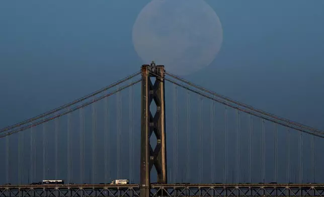 The Harvest Supermoon descends behind the Bay Bridge as seen from Alameda, Calif., Tuesday, Oct. 7, 2025. (AP Photo/Godofredo A. Vásquez)