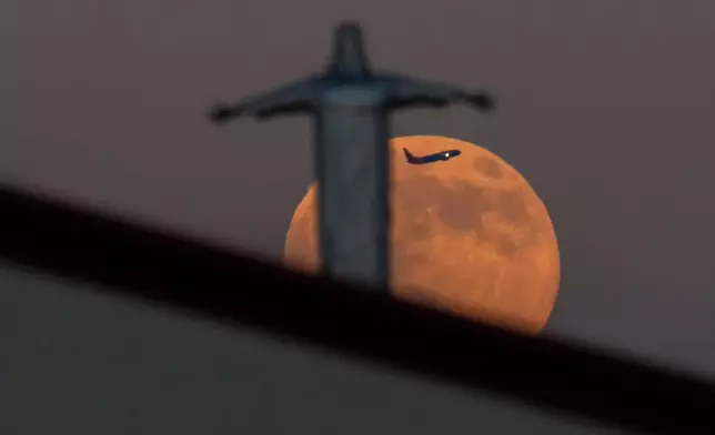 A Southwest Airlines plane appears between the Harvest Supermoon and a statue of Jesus Christ atop Iglesia Luterana Santa Maria de Guadalupe as it takes off from Dallas Love Field Airport, Monday, Oct. 6, 2025, in Irving, Texas. (AP Photo/Julio Cortez)