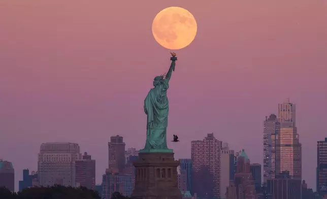 The Harvest Supermoon rises behind the Statue of Liberty and the Brooklyn skyline, Monday, Oct. 6, 2025, in Jersey City, N.J. (AP Photo/Adam Gray)