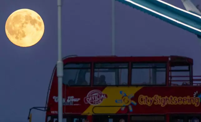 The Harvest Supermoon rises as a red double-decker bus drives past on Tower Bridge, Monday, Oct. 6, 2025, in London. (AP Photo/Julia Demaree Nikhinson)