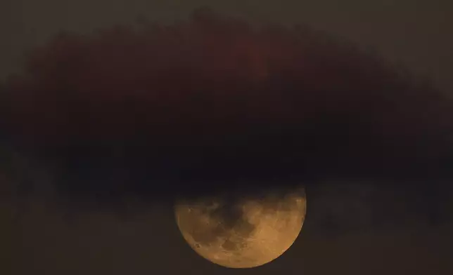 The full Harvest Moon rises behind a cloud in the sky in Hadera, Israel, Monday, Oct. 6, 2025. (AP Photo/Ariel Schalit)