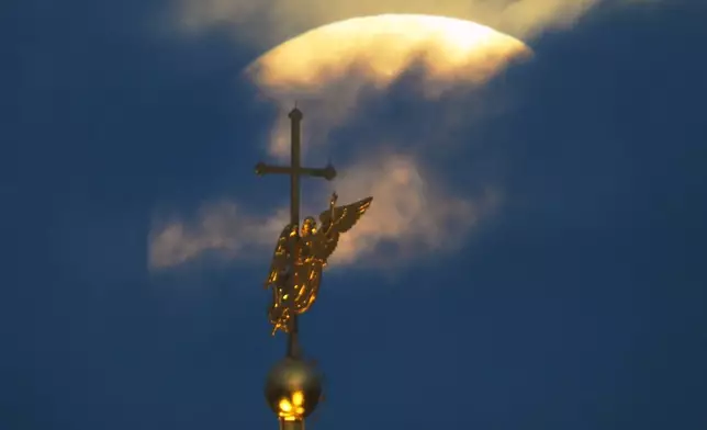 The Harvest Supermoon sets in the clouds behind the city landmark, a weather vane in the form of an angel fixed atop a spire of the Saints Peter and Paul Cathedral in St. Petersburg, Russia, early Tuesday, Oct. 7, 2025. (AP Photo/Dmitri Lovetsky)