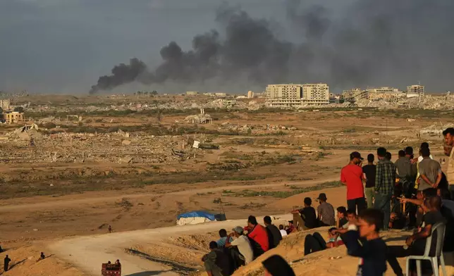 Displaced Palestinians watch smoke rise after Israeli military strikes as they gather on the coastal road near Wadi Gaza, in the central Gaza Strip, Thursday, Oct. 9, 2025. (AP Photo/Abdel Kareem Hana)