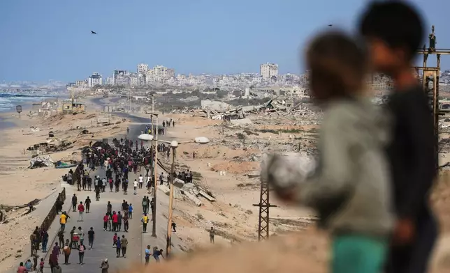 Displaced Palestinians gather on the coastal road near Wadi Gaza after the announcement that Israel and Hamas had agreed to the first phase of a peace plan to pause the fighting, as Israeli tanks block the road leading to Gaza City, in the central Gaza Strip, Thursday, Oct. 9, 2025. (AP Photo/Abdel Kareem Hana)