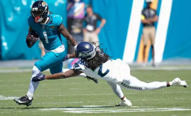 Jacksonville Jaguars running back Travis Etienne (1) tries to escape a tackle by Seattle Seahawks cornerback Shaquill Griffin (24) during the first half of an NFL football game Sunday, Oct. 12 2025, in Jacksonville, Fla. (AP Photo/John Raoux)