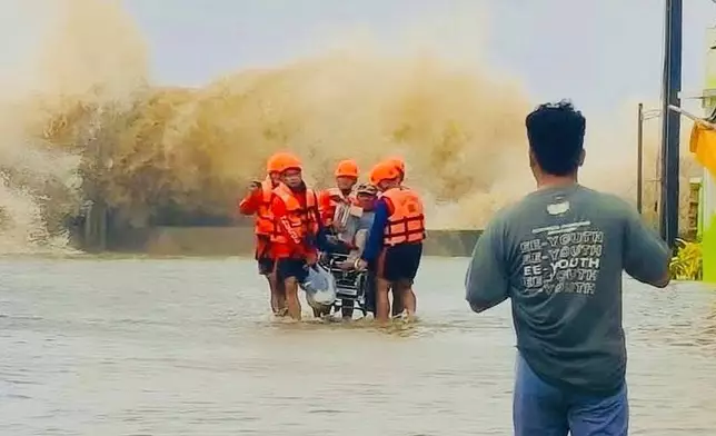 In this photo provided by the Philippine Coast Guard, rescuers evacuate a resident on a wheelchair as waves batter due to Tropical Storm Bualoi in San Agustin, Romblon province, Philippines on Friday Sept. 26, 2025. (Philippine Coast Guard via AP)