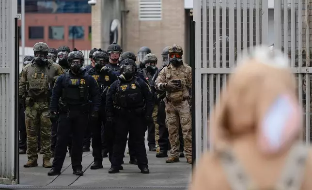 Law enforcement officers watch as the gates close at a U.S. Immigration and Customs Enforcement facility as people protest outside on Saturday, Oct. 11, 2025, in Portland, Ore. (AP Photo/Jenny Kane)