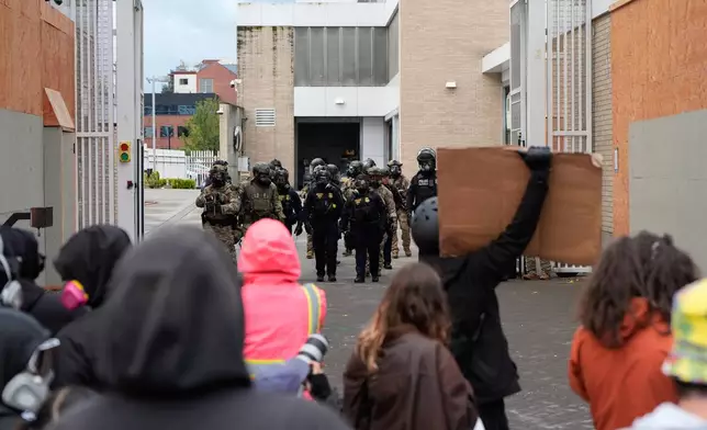 Law enforcement officers walk back to a U.S. Immigration and Customs Enforcement facility as people protest on Saturday, Oct. 11, 2025, in Portland, Ore. (AP Photo/Jenny Kane)