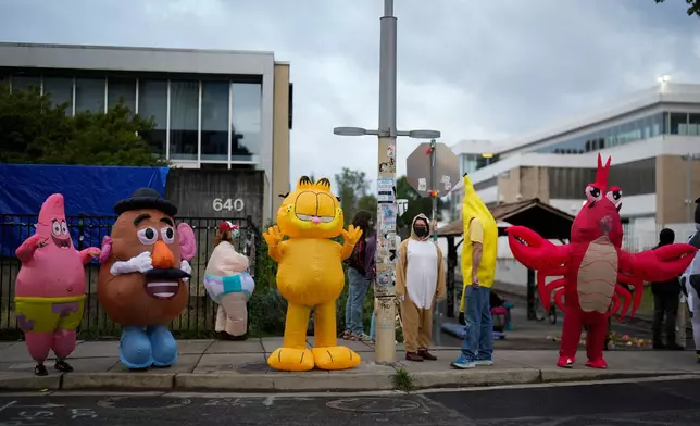 People wearing costumes protest outside a U.S. Immigration and Customs Enforcement facility, at right, on Saturday, Oct. 11, 2025, in Portland, Ore. (AP Photo/Jenny Kane)