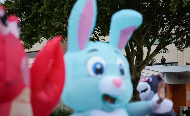 Law enforcement officers watch from a ledge on the a U.S. Immigration and Customs Enforcement facility, at right, as people in costumes protest on Saturday, Oct. 11, 2025, in Portland, Ore. (AP Photo/Jenny Kane)
