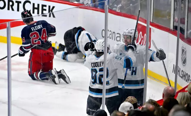 Utah Mammoth's Dylan Guenther (11) celebrates after the winning goal against the Winnipeg Jets with Logan Cooley (92) during the third period of an NHL hockey game in Winnipeg, Manitoba, Sunday, Oct. 26, 2025. (Fred Greenslade/The Canadian Press via AP)