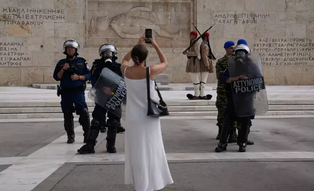 A woman takes a snapshot at the Greek parliament as Greek police stand guard near a protest during a nationwide 24-hour strike in Athens, Greece, Wednesday, Oct. 1, 2025. (AP Photo/Petros Giannakouris)