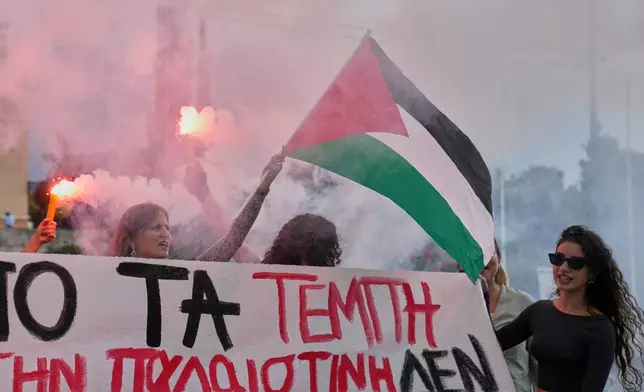Protesters with flares wave a Palestinian flag during a nationwide 24-hour strike, as labor unions demand higher wages and the withdrawal of a bill that changes work hours Wednesday, Oct. 1, 2025. (AP Photo/Petros Giannakouris)