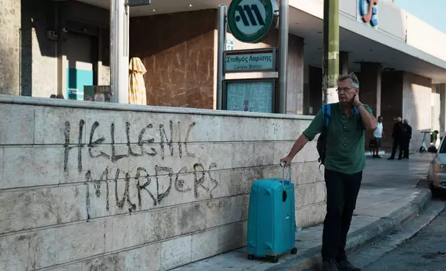 A traveler stands outside the closed main railway station during a nationwide 24-hour strike, as labor unions demand higher wages and the withdrawal of a bill that changes work hours in Athens, Greece, Wednesday, Oct. 1, 2025. (AP Photo/Thanassis Stavrakis)