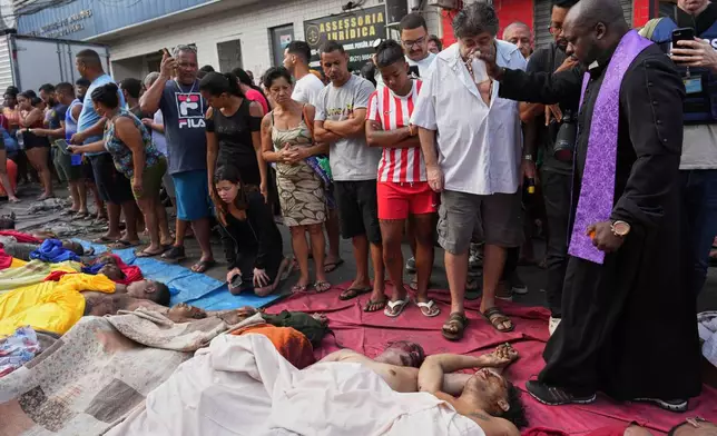 A priest blesses the bodies of people killed the day before during a police raid targeting the Comando Vermelho gang in the Complexo da Penha favela of Rio de Janeiro, Brazil, Wednesday, Oct. 29, 2025. (AP Photo/Silvia Izquierdo)