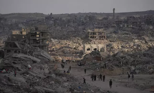 Palestinians walk among destroyed buildings in Gaza City, Sunday, Oct. 12, 2025, after Israel and Hamas agreed to a pause in their war and the release of the remaining hostages. (AP Photo/Jehad Alshrafi)