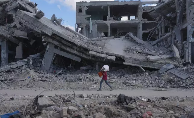 A Palestinian carries belongings while walking past destroyed buildings in Gaza City, Sunday, Oct. 12, 2025, after Israel and Hamas agreed to a pause in their war and the release of the remaining hostages. (AP Photo/Jehad Alshrafi)