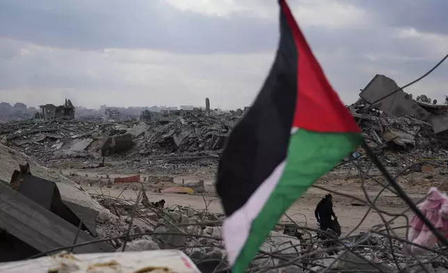 A displaced man walks past a Palestinian flag placed over the rubble of destroyed buildings in Gaza City, Sunday, Oct. 12, 2025, after Israel and Hamas agreed to a temporary pause in their war and the release of the remaining hostages. (AP Photo/Abdel Kareem Hana)