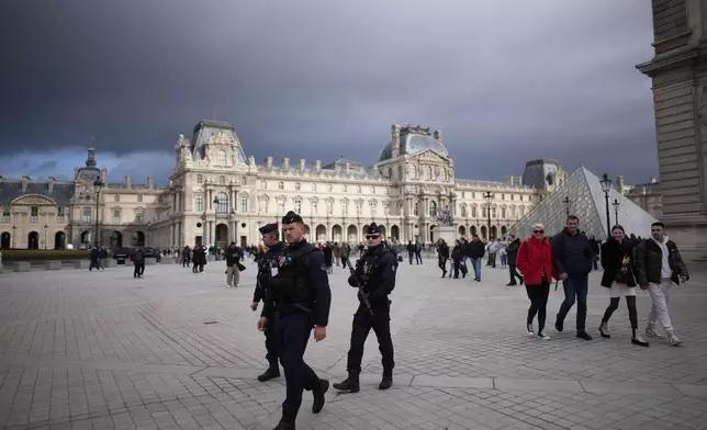 Riot police officers patrol as people stroll in Le Louvre museum courtyard, Monday, Oct. 27, 2025 in Paris. (AP Photo/Christophe Ena)