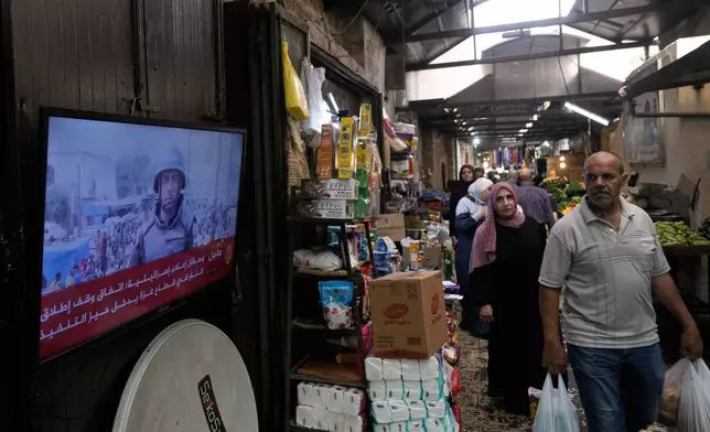 A Palestinian man looks at a television broadcasting the news following the announcement that Israel and Hamas have agreed to the first phase of a peace plan to pause the fighting, as he walks at a local market in the Old City of Nablus, in the West Bank, Thursday, Oct. 9, 2025. (AP Photo/Majdi Mohammed)