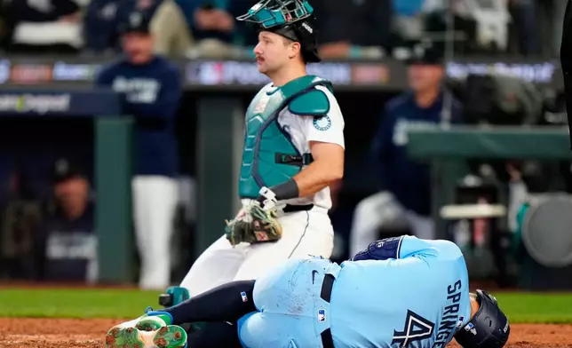 Toronto Blue Jays outfielder George Springer (4) rolls on the ground after taking a pitch to the knee from Seattle Mariners pitcher Bryan Woo (22) during seventh inning MLB Game 5 of baseball's American League Championship Series action in Seattle, Friday, Oct. 17, 2025. (Frank Gunn/The Canadian Press via AP)