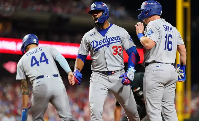 Los Angeles Dodgers' Teoscar Hernández, center, reacts with Will Smith, right, after hitting a three-run home run against Philadelphia Phillies pitcher Matt Strahm during the seventh inning in Game 1 of baseball's National League Division Series, Saturday, Oct. 4, 2025, in Philadelphia. (AP Photo/Matt Slocum)
